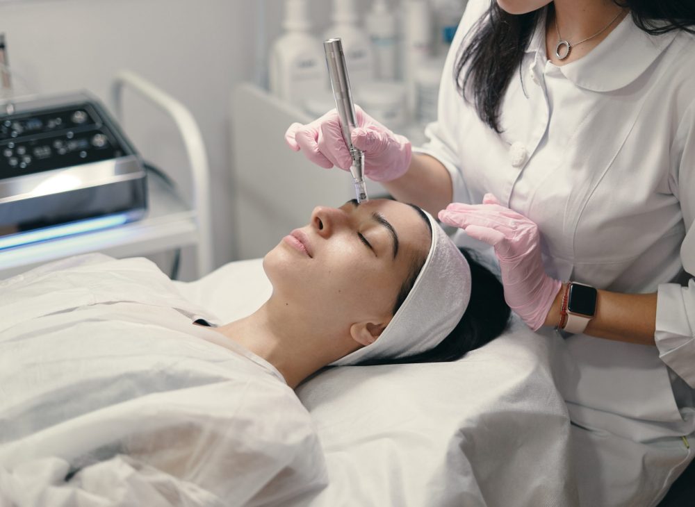 Model with closed eyes and hand's of doctor. Rejuvenating facial treatment. Model getting lifting therapy massage in a beauty SPA salon. Cosmetological clinic, procedure.