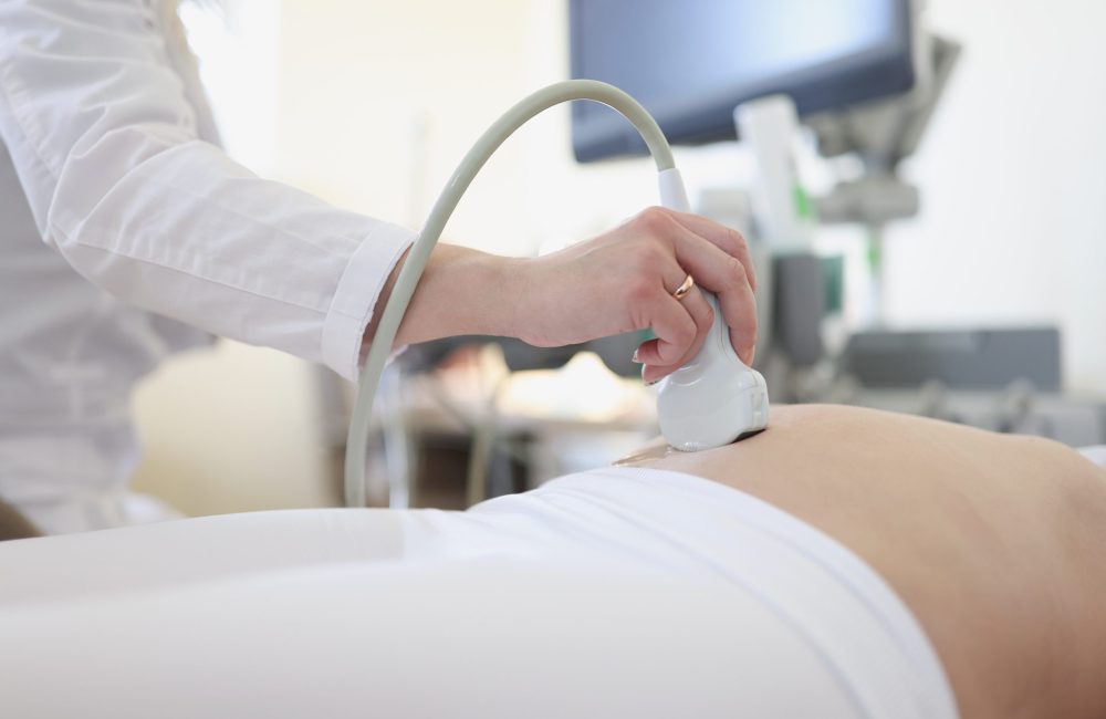 Ultrasound scanner device in hand of professional doctor examining his patient. Doing abdominal ultrasound scanning sonogram early pregnancy