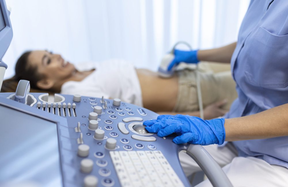 Ultrasound diagnostic of stomach on abdominal to woman in clinic, closeup view. Doctor runs ultrasound sensor over patient's girl tummy and looks at image on screen. Diagnosis of internal organs.
